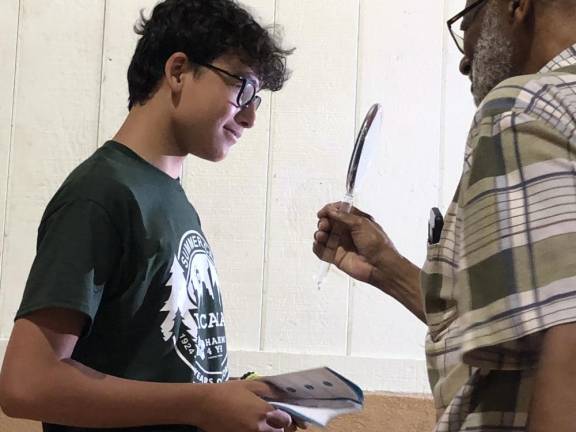 Optician Floyd Patterson holds up a mirror for Maxim Reyes to see his new glasses.