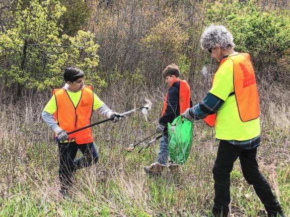 Jayden Cibenko, 11, drops trash in a bag held by Bob Manning. At center is Joseph Bosland, 12.