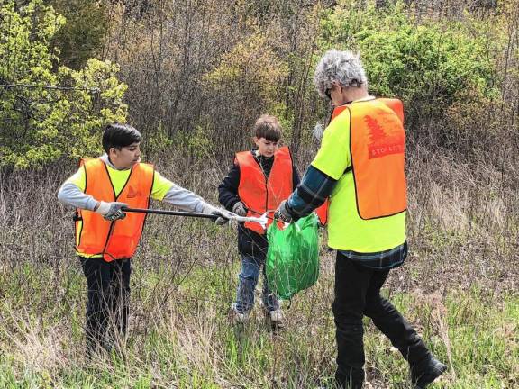 Jayden Cibenko, 11, drops trash in a bag held by Bob Manning. At center is Joseph Bosland, 12.