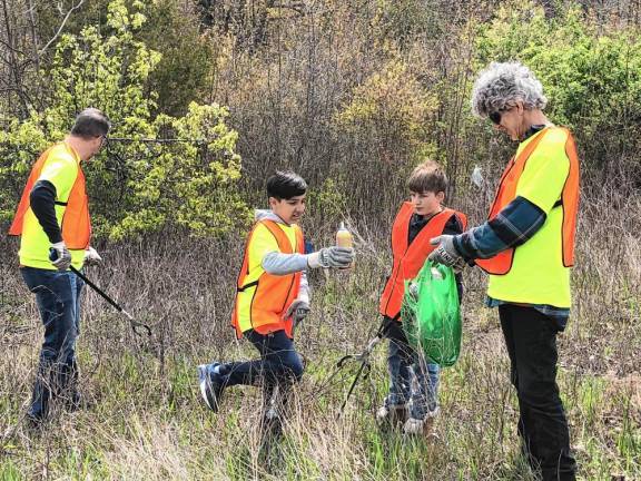 Jayden Cibenko, 11, drops a whip cream can in a bag held by Bob Manning. With them are Daniel Cibenko, left, and Joseph Bosland, 12. They were one of the teams from the Almond Branch Church taking part in West Milford’s Beautification Day on Saturday, April 27. They were collecting trash along Lincoln Avenue. (Photo by Kathy Shwiff)