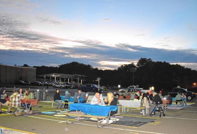 Residents dine at tables in the high school parking lot.