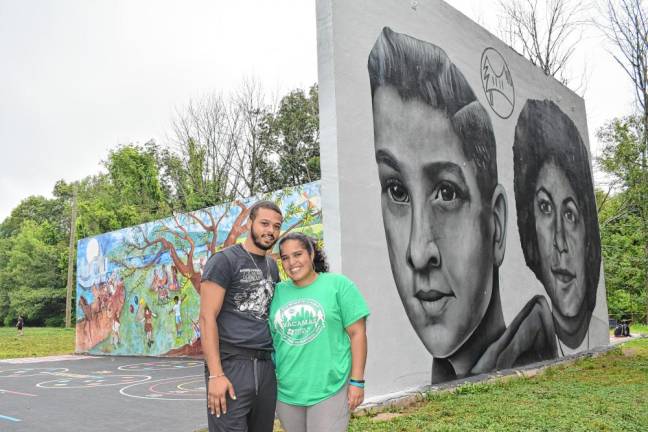 Francisco Emeterio, a former camper and current staff member of Camp Vacamas, and Jasmine Caraballo, division head for day campers, stand before a mural dedicated to Hands in 4 Youth board members Dennis Tarnow and Annette Leder, who were campers in the 1950s and ’60s.