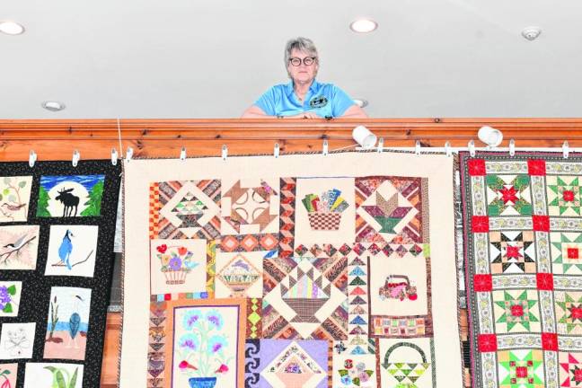 QT3 Meg Woznicki of Oak Ridge stands above quilts on display Saturday, March 16 at the West Milford Museum.