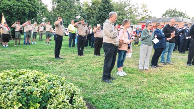 Boy Scouts and veterans salute during the ceremony as residents and council members hold candles.